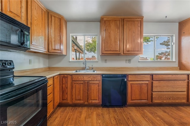 kitchen featuring light countertops, brown cabinetry, a sink, and black appliances