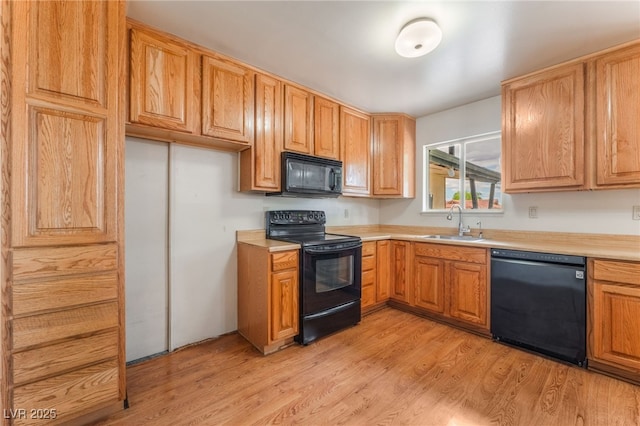kitchen with light wood-type flooring, a sink, black appliances, and light countertops