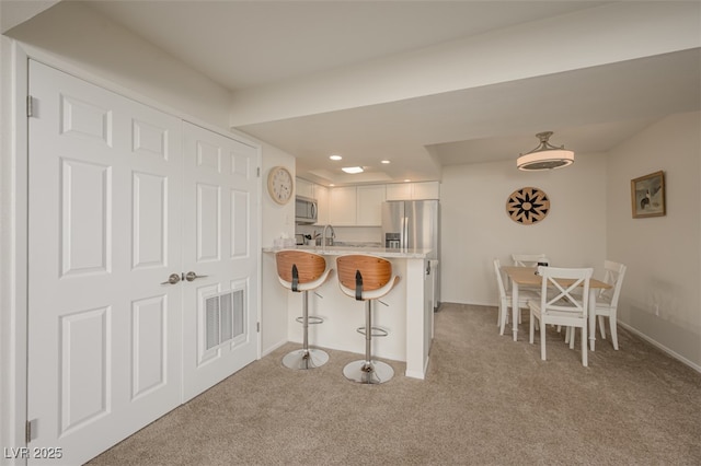 kitchen featuring a breakfast bar area, visible vents, light colored carpet, light countertops, and stainless steel appliances