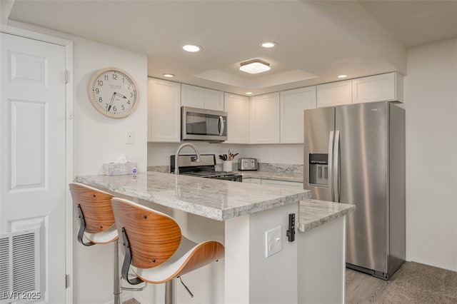 kitchen with a peninsula, light stone countertops, recessed lighting, white cabinetry, and stainless steel appliances