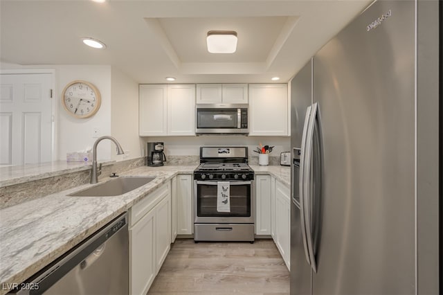 kitchen with white cabinets, stainless steel appliances, a sink, and a raised ceiling