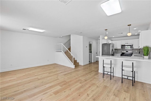 kitchen featuring stainless steel appliances, white cabinetry, light wood finished floors, and a peninsula