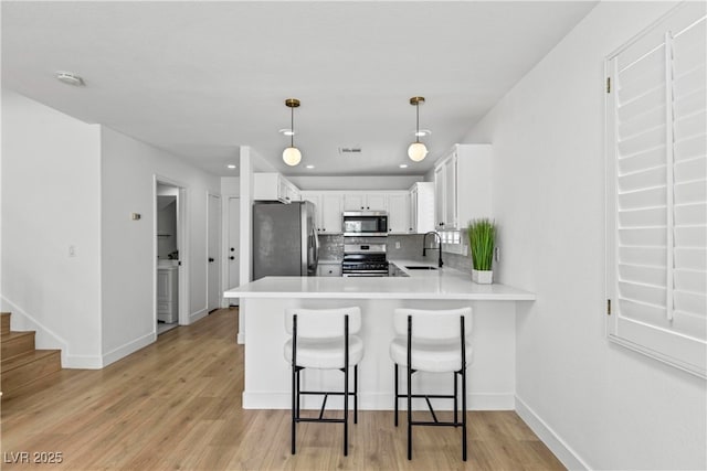 kitchen with white cabinets, a sink, light wood finished floors, stainless steel appliances, and a peninsula