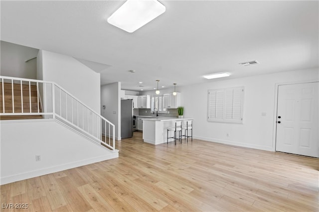 unfurnished living room featuring visible vents, stairs, baseboards, a sink, and light wood-style flooring