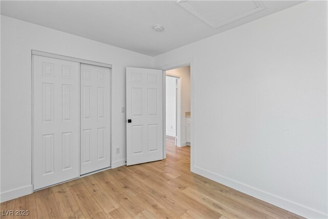 unfurnished bedroom with baseboards, a closet, attic access, and light wood-style flooring