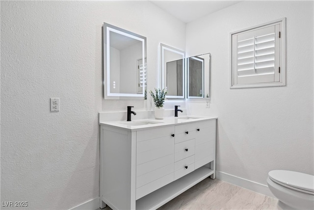 bathroom with a sink, baseboards, toilet, and double vanity