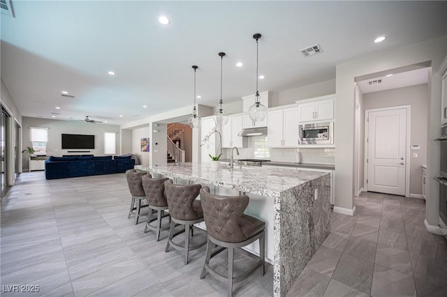 12018 Vento Forte Ave, Las Vegas, NV 89138 - kitchen featuring under cabinet range hood, stainless steel microwave, a large island, open floor plan, and recessed lighting