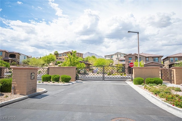 12018 Vento Forte Ave, Las Vegas, NV 89138 - view of asphalt road featuring a gate, a residential view, curbs, a gated entry, and street lights