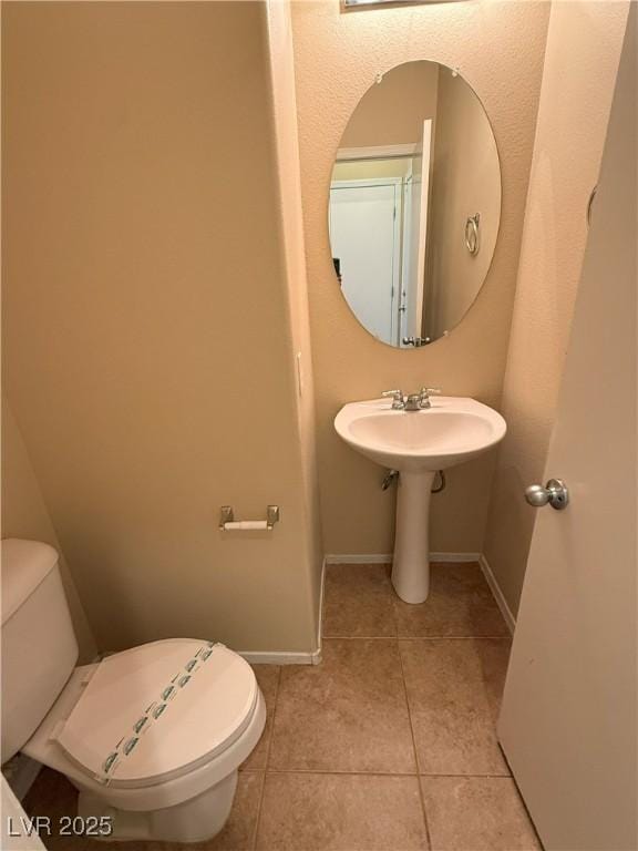 half bathroom with a sink, baseboards, tile patterned flooring, and toilet