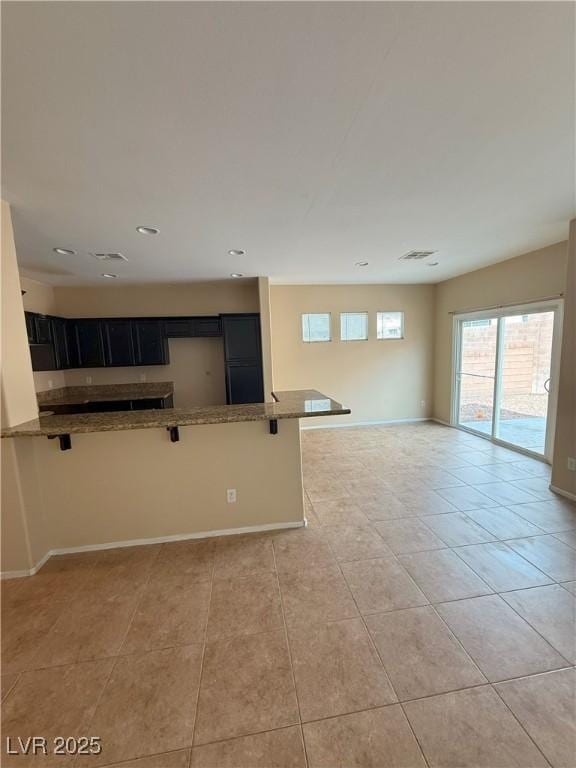 kitchen with dark cabinets, light tile patterned floors, stone counters, a breakfast bar, and recessed lighting