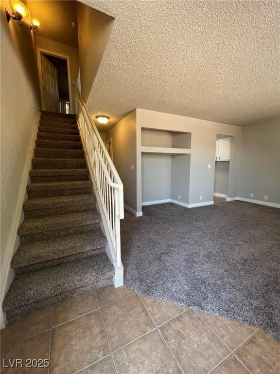 stairway featuring baseboards, carpet flooring, and a textured ceiling
