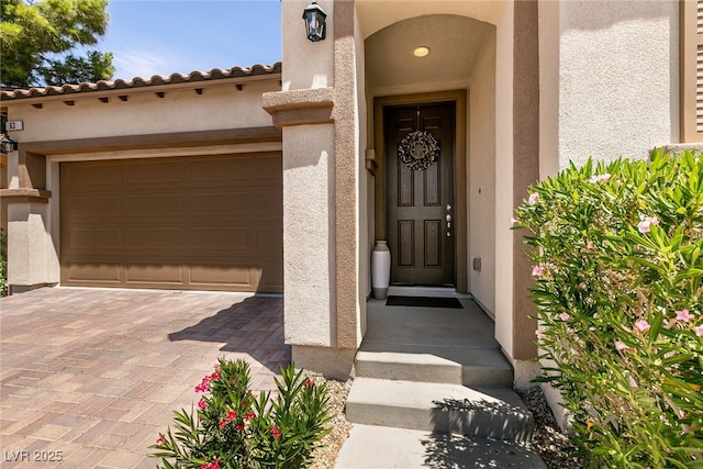 property entrance with an attached garage, decorative driveway, and stucco siding