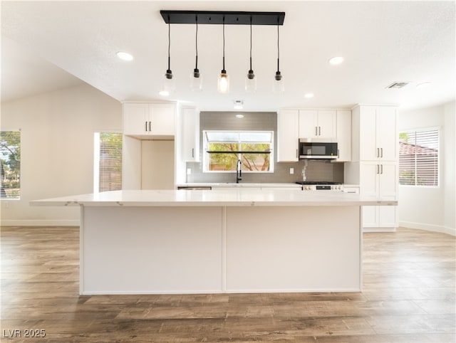 2505 Showcase Dr, Las Vegas, NV 89134 - kitchen with stainless steel microwave, baseboards, a center island, white cabinetry, and decorative backsplash