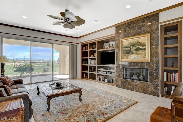 living area featuring crown molding, a fireplace, a ceiling fan, and built in shelves