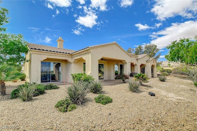 rear view of property featuring a tiled roof, ceiling fan, a chimney, a patio area, and stucco siding