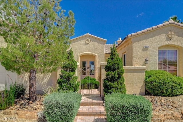 property entrance with a tile roof, fence, a gate, and stucco siding