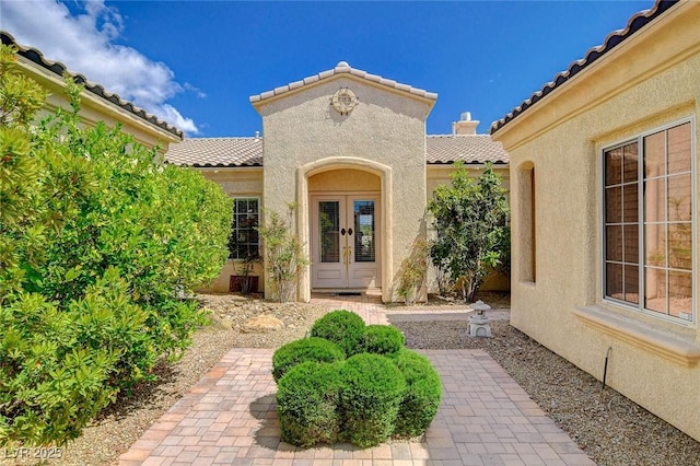 view of exterior entry with french doors, stucco siding, and a tile roof