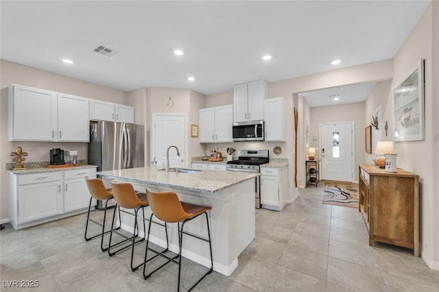 kitchen with visible vents, a breakfast bar area, white cabinets, a sink, and appliances with stainless steel finishes