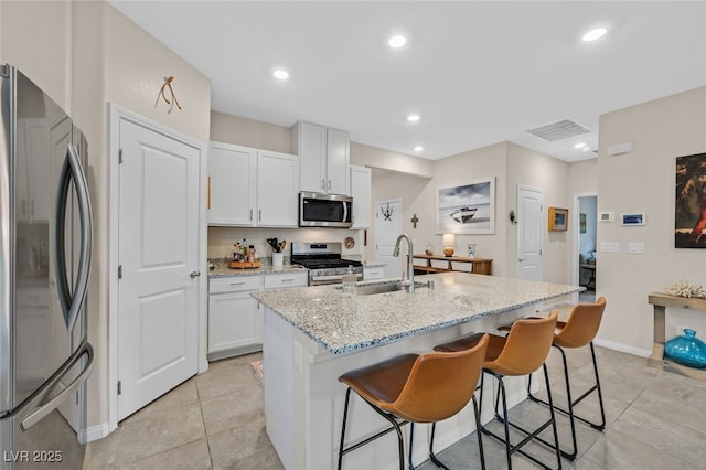 kitchen featuring a breakfast bar area, appliances with stainless steel finishes, light stone countertops, a sink, and white cabinetry