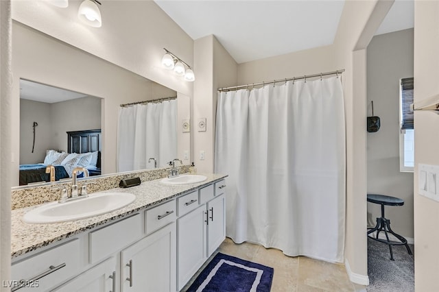 full bath featuring double vanity, a sink, connected bathroom, and baseboards