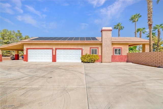 view of front of property featuring a chimney, solar panels, concrete driveway, an attached garage, and stucco siding