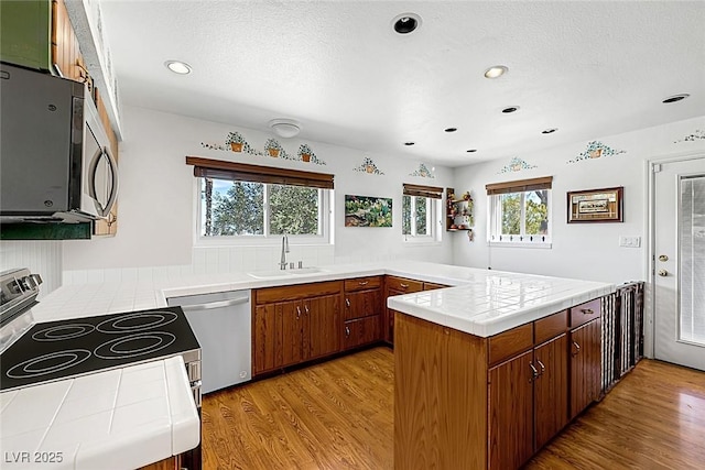 kitchen with tile countertops, appliances with stainless steel finishes, a sink, light wood finished floors, and a peninsula