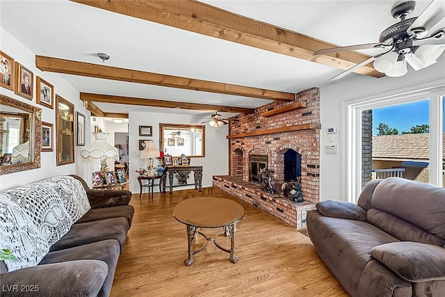 living room with light wood-style floors, ceiling fan, a fireplace, and beamed ceiling