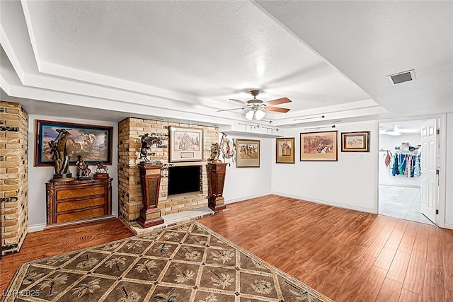 unfurnished living room with a ceiling fan, a tray ceiling, visible vents, and wood finished floors