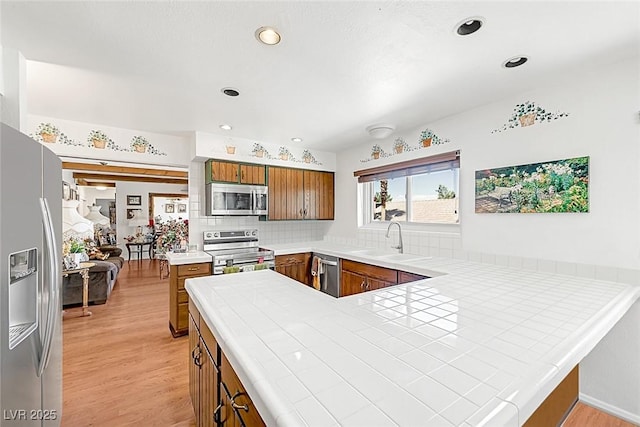 kitchen featuring brown cabinets, a sink, stainless steel appliances, a peninsula, and light wood-type flooring