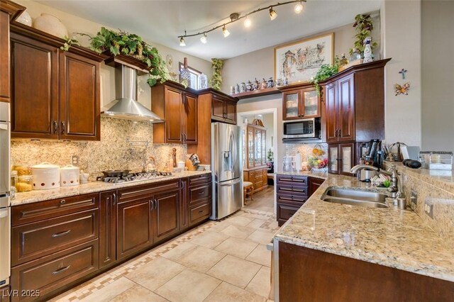 kitchen featuring decorative backsplash, wall chimney range hood, light stone counters, a sink, and appliances with stainless steel finishes