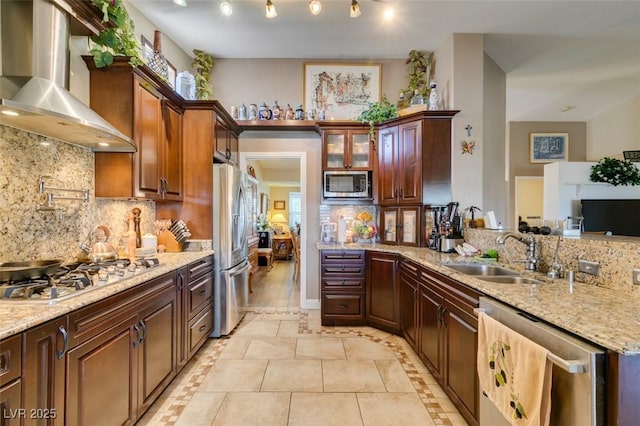 kitchen with decorative backsplash, wall chimney range hood, light stone counters, a sink, and appliances with stainless steel finishes