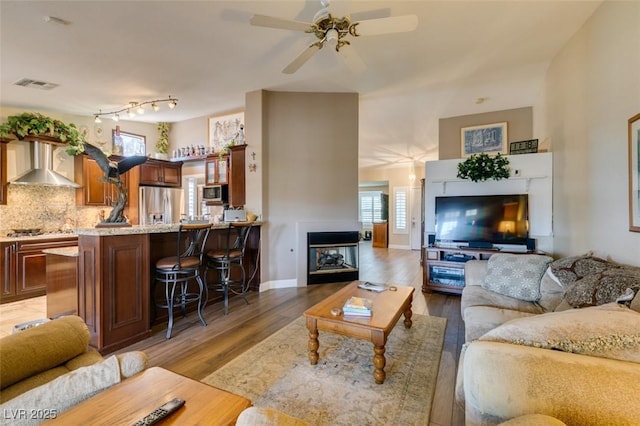 living area featuring a wealth of natural light, light wood-style flooring, ceiling fan, and visible vents