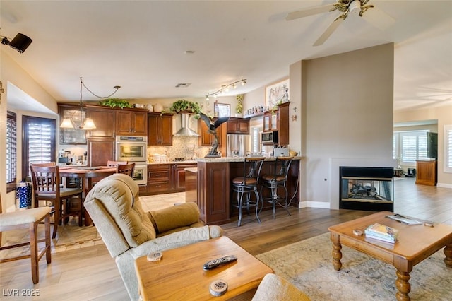 living room with a ceiling fan, baseboards, visible vents, and light wood finished floors