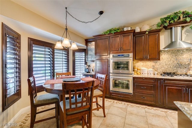 kitchen with decorative backsplash, pendant lighting, light stone countertops, wall chimney range hood, and stainless steel appliances
