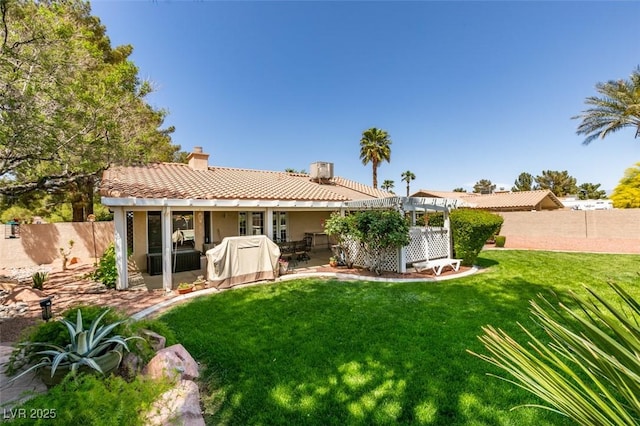 rear view of house featuring a tiled roof, a lawn, a chimney, and a fenced backyard