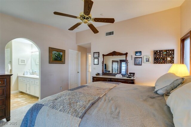 bedroom with ceiling fan, visible vents, arched walkways, ensuite bathroom, and light carpet