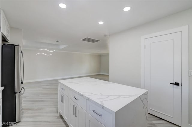 kitchen with white cabinets, freestanding refrigerator, a kitchen island, and light stone countertops