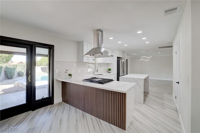 kitchen featuring visible vents, freestanding refrigerator, baseboards, island range hood, and cooktop