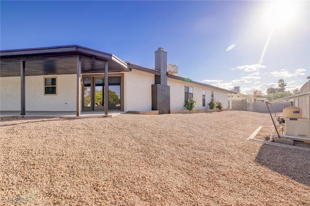 back of property with stucco siding, a chimney, and a patio area
