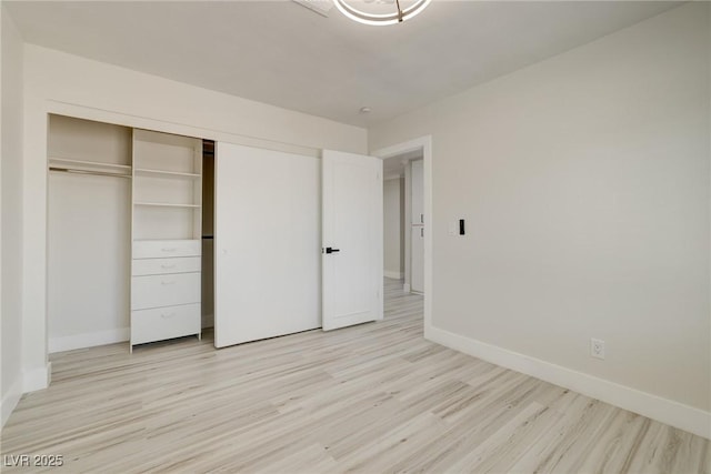 unfurnished bedroom featuring baseboards, light wood finished floors, and a closet