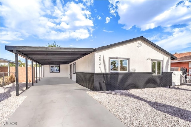 view of front of home with fence, brick siding, stucco siding, a carport, and driveway