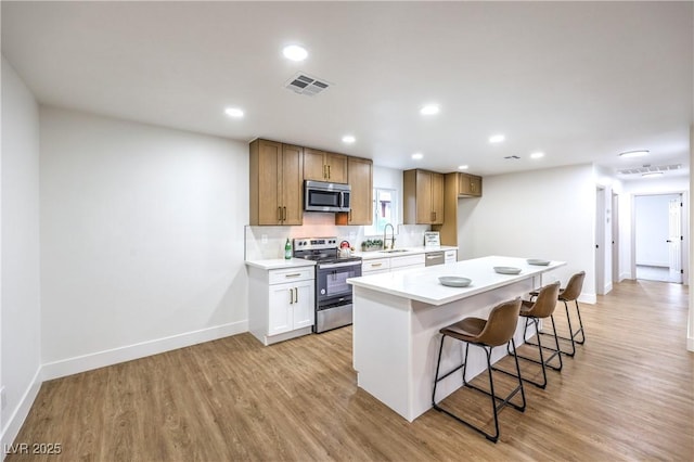 kitchen featuring a breakfast bar, a sink, stainless steel appliances, baseboards, and light wood-type flooring