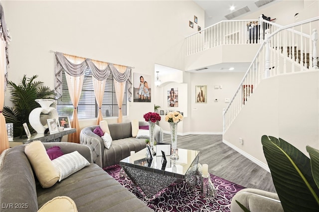 living area with stairway, baseboards, wood finished floors, and a towering ceiling