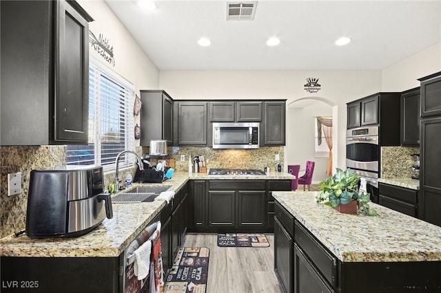 kitchen featuring visible vents, light wood-style floors, a center island, a sink, and stainless steel appliances