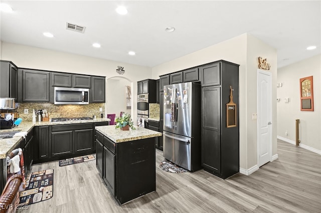 kitchen with a center island, decorative backsplash, light wood finished floors, and stainless steel appliances