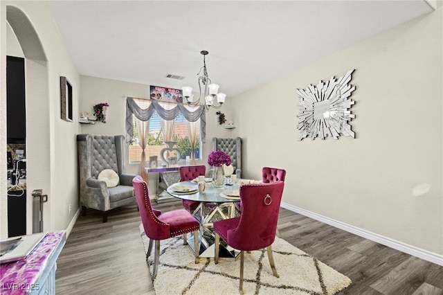 dining area with visible vents, wood finished floors, baseboards, a chandelier, and arched walkways