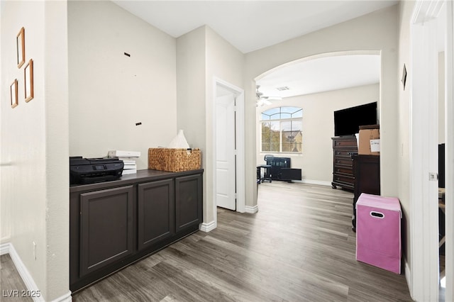 corridor with arched walkways, baseboards, and wood finished floors