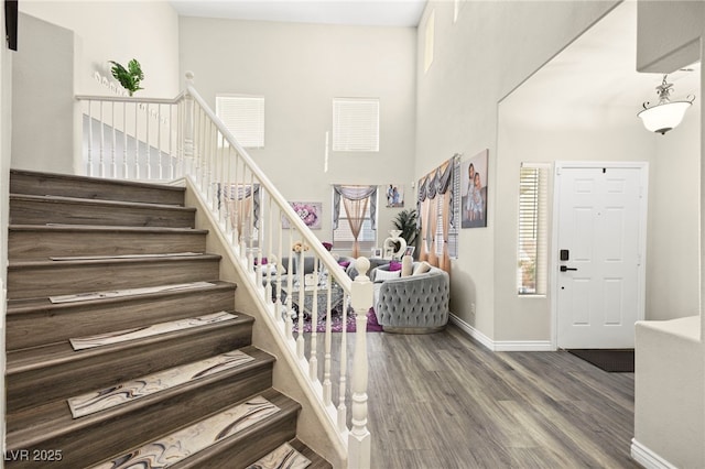 foyer featuring baseboards, a high ceiling, stairs, and wood finished floors