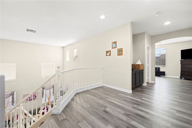 corridor with arched walkways, recessed lighting, baseboards, wood finished floors, and visible vents