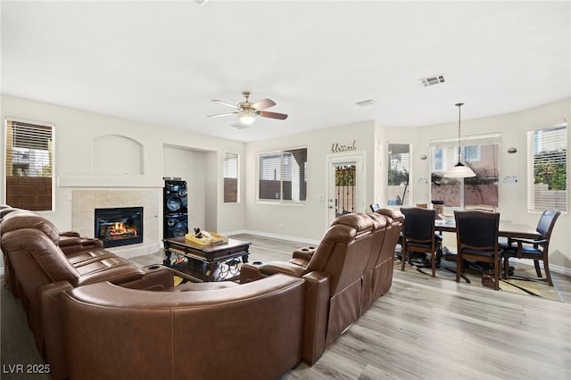 living room featuring a ceiling fan, baseboards, a tiled fireplace, and light wood-type flooring